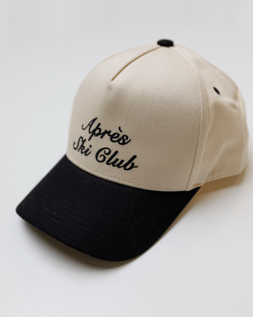 Cream colored trucker hat with a black bill and black embroidery that says "Apres Ski Club" on a white background