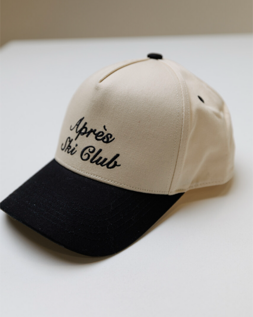 Cream colored trucker hat with a black bill and black embroidery that says "Apres Ski Club" on a white background