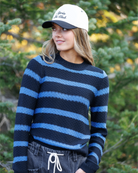 Woman standing in forest wearing a black and white hat with a black and blue striped sweater