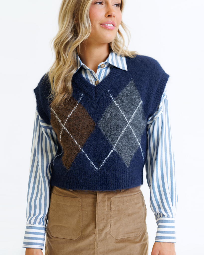 Woman wearing a blue sweater vest over a striped shirt on a white background