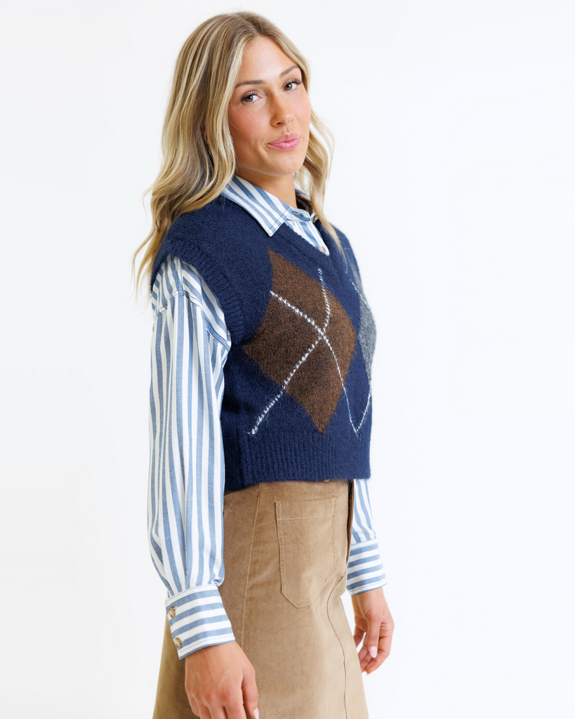 Woman wearing a blue sweater vest over a striped shirt on a white background