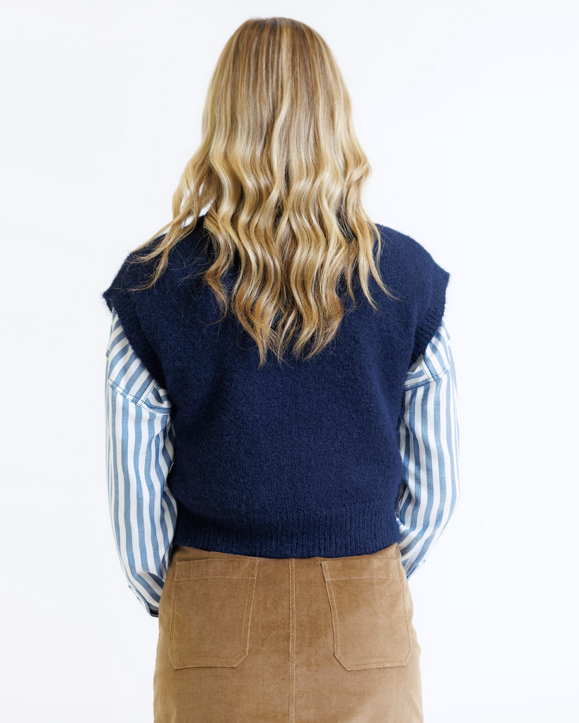 Woman wearing a blue sweater vest over a striped shirt on a white background