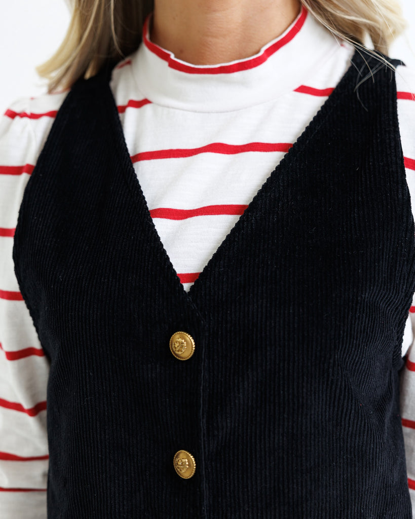 Black corduroy vest with gold buttons over a red and white striped shirt.