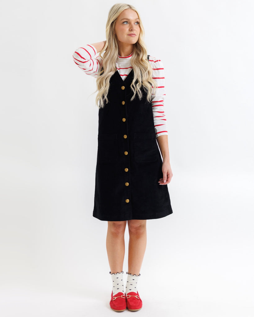 Woman wearing a black dress with gold buttons and a red and white striped shirt on a white background