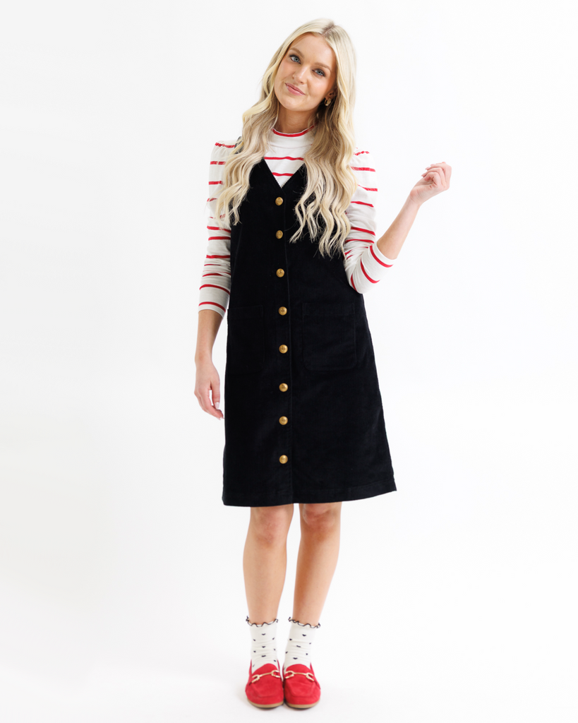 Woman wearing a black dress with gold buttons and a red and white striped shirt on a white background