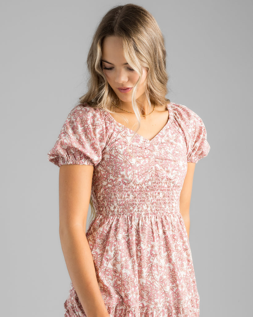 Model wearing a pink floral print, short sleeve, sweetheart neckline with smocked bodice, midi-length dress.