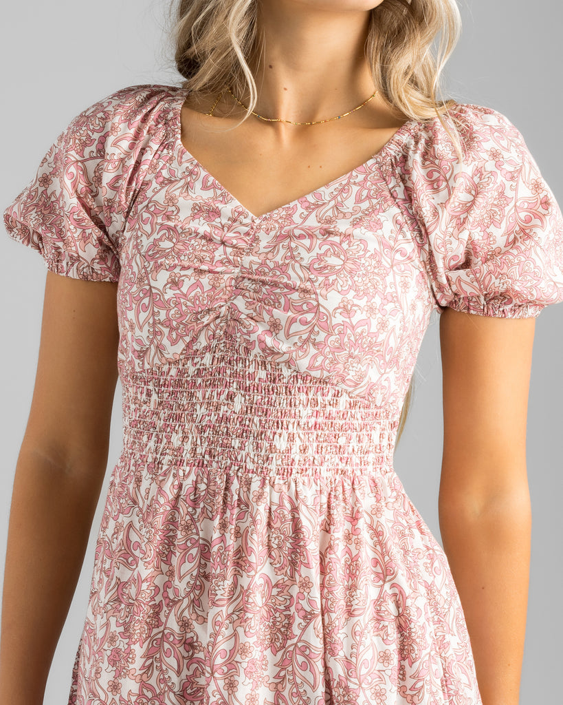 Model wearing a pink floral print, short sleeve, sweetheart neckline with smocked bodice, midi-length dress.