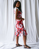 Woman wearing a red floral dress standing against a white curtain.