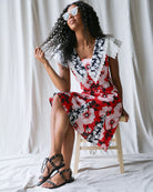 Woman in a colorful dress sitting on a stool against a white curtain background