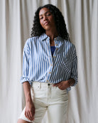 Woman wearing a blue and white striped shirt and white pants against a plain background