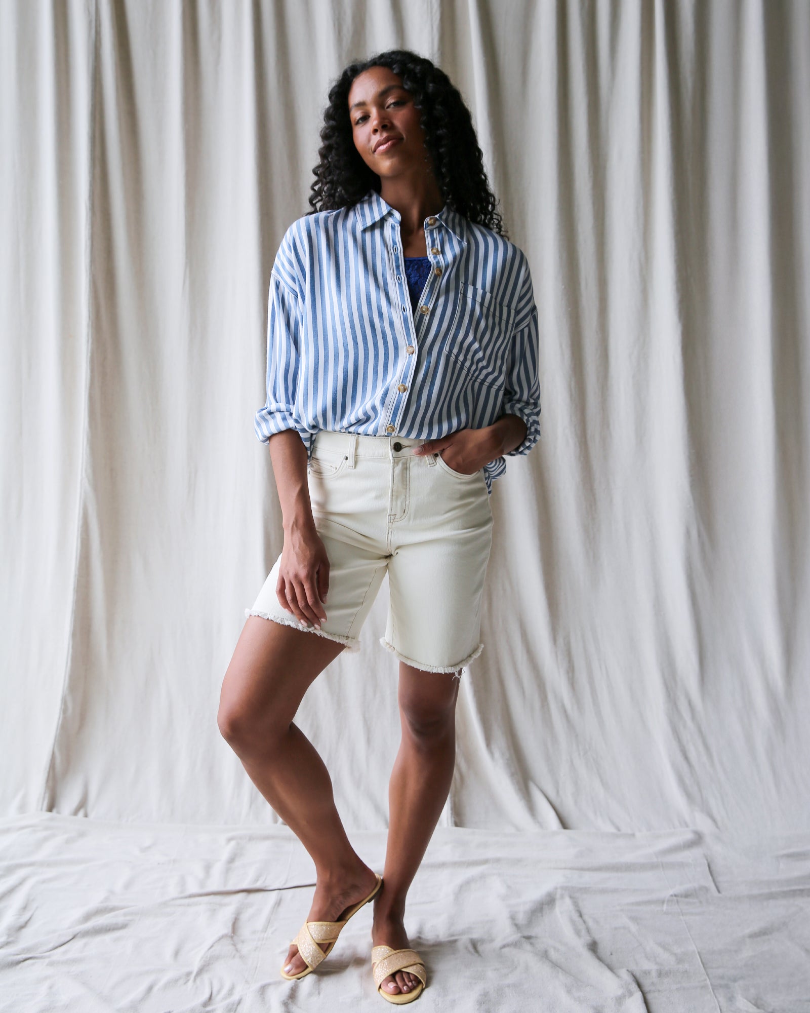 Woman wearing a striped shirt and white shorts against a white curtain background
