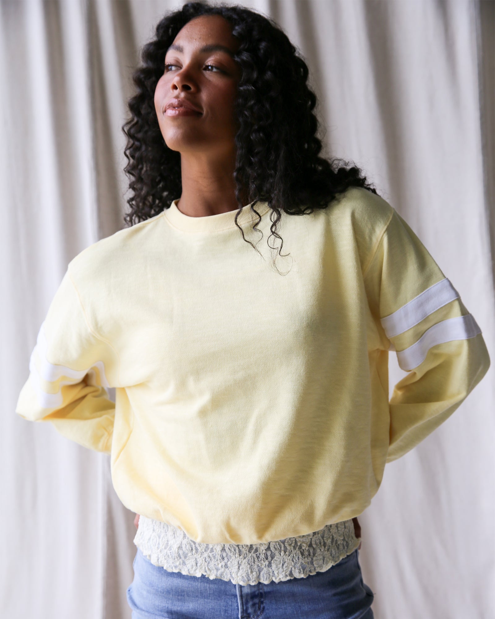 Woman wearing a light yellow sweatshirt with white stripes on sleeves against a plain background