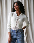 Woman wearing a white cardigan with lace details against a plain background