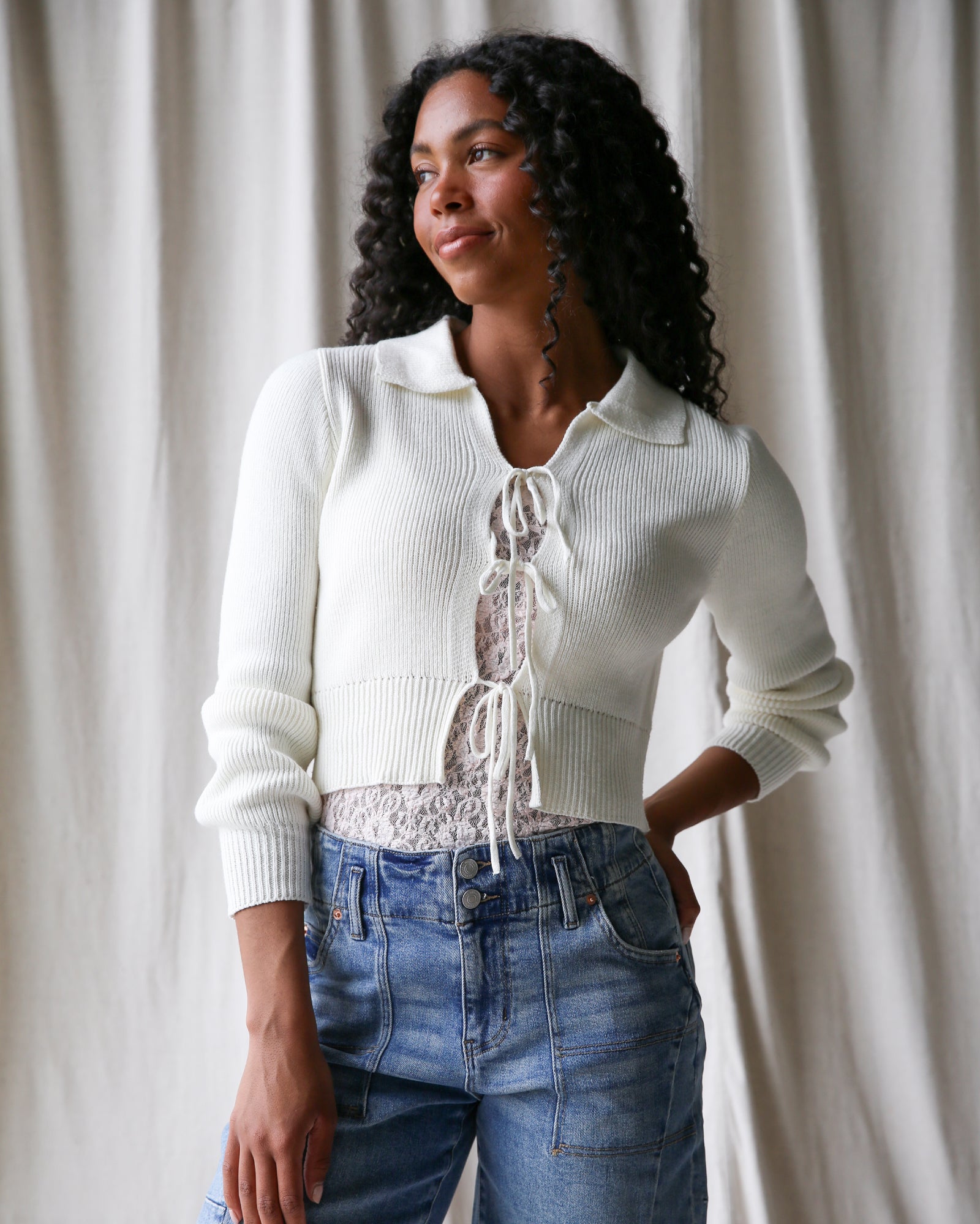 Woman wearing a white cardigan with lace details against a plain background