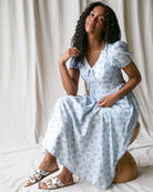 Woman wearing a light blue floral dress sitting on a white surface with a neutral background