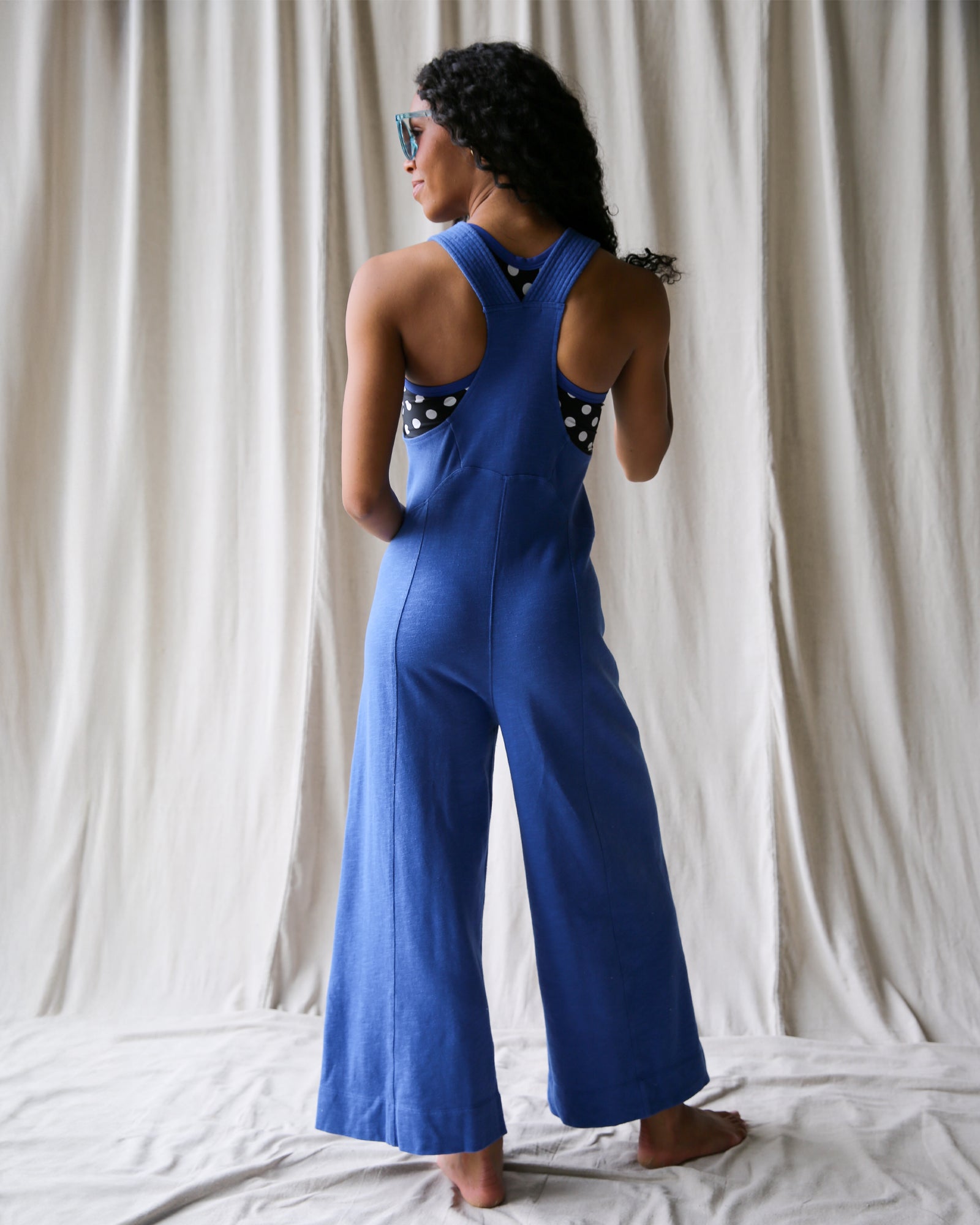 Person wearing a blue jumpsuit with white polka dots in front of a white curtain.