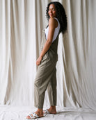 Woman wearing a green jumpsuit against a white curtain background