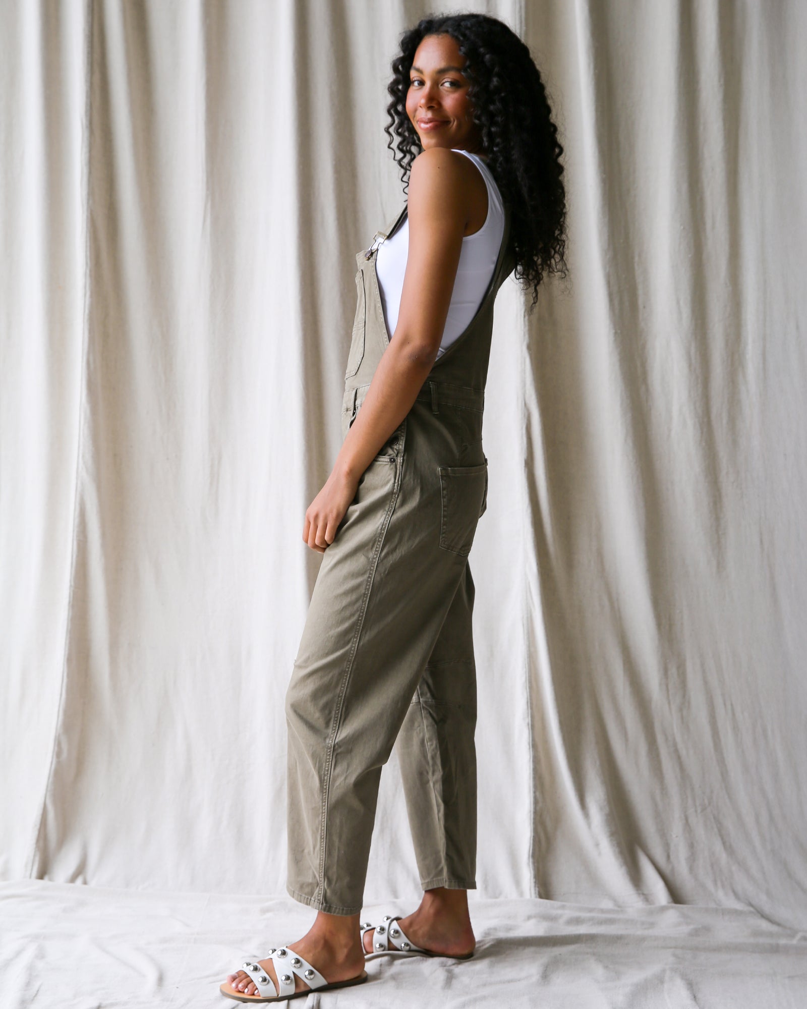 Woman wearing a green jumpsuit against a white curtain background