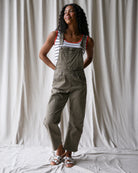 Woman wearing green overalls standing against a white curtain