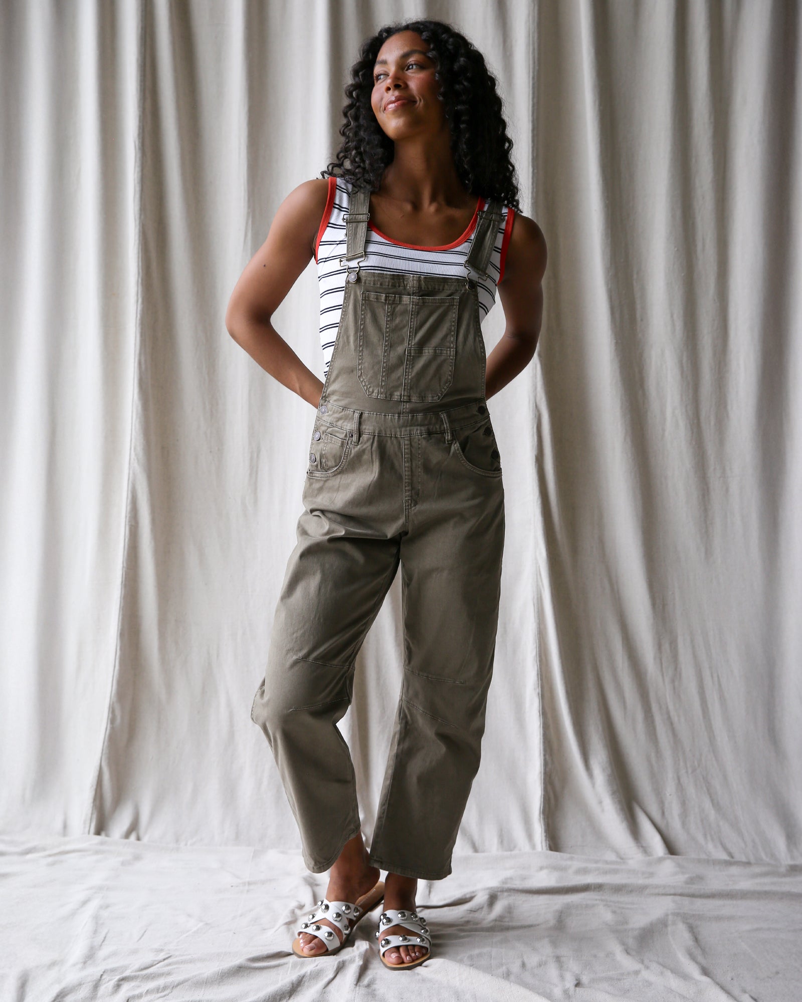 Woman wearing green overalls standing against a white curtain