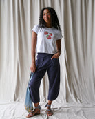 Woman wearing a white t-shirt with red floral design and dark blue pants, standing against a plain background.