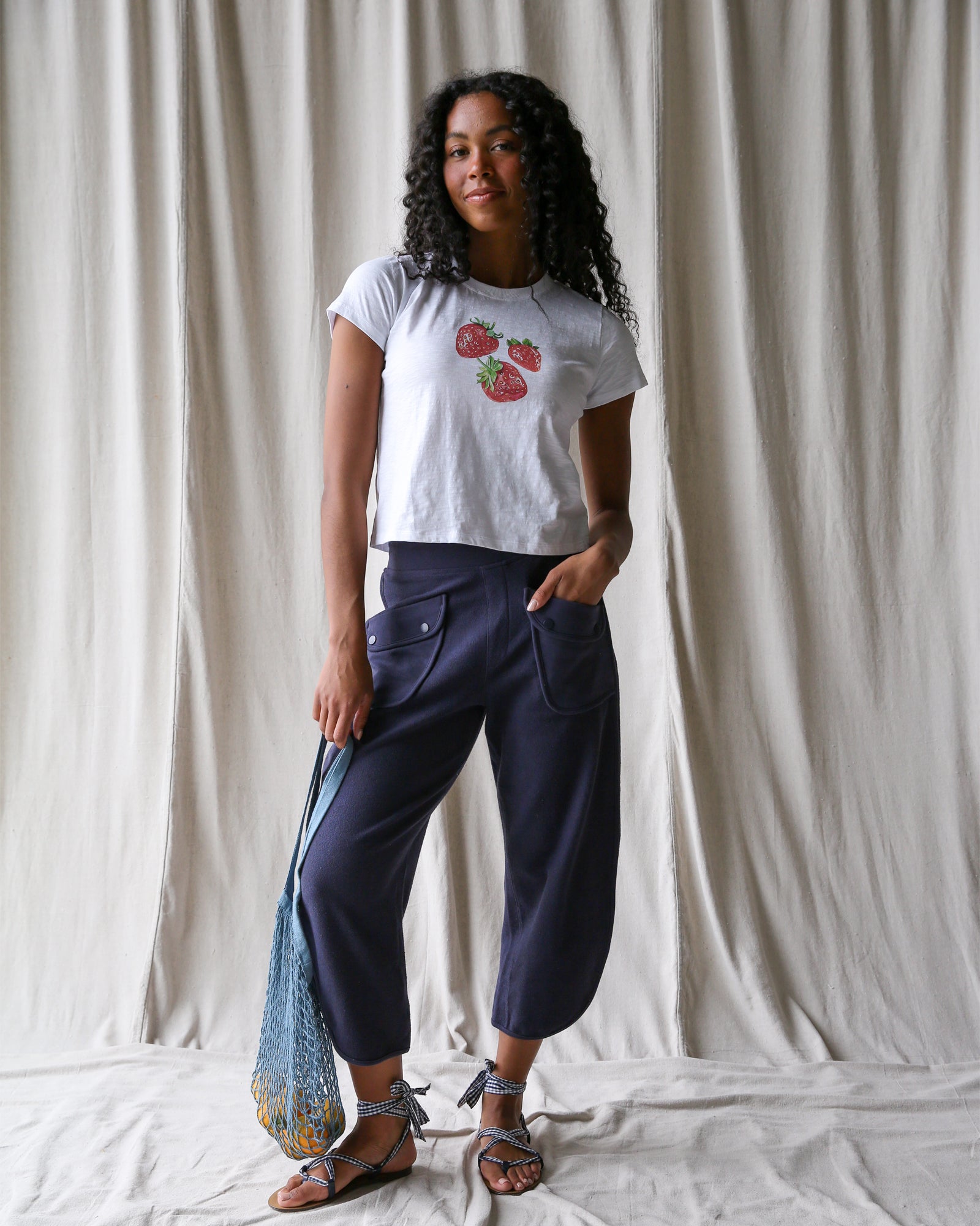 Woman wearing a white t-shirt with red floral design and dark blue pants, standing against a plain background.