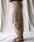 Person wearing beige cargo pants standing against a white curtain background
