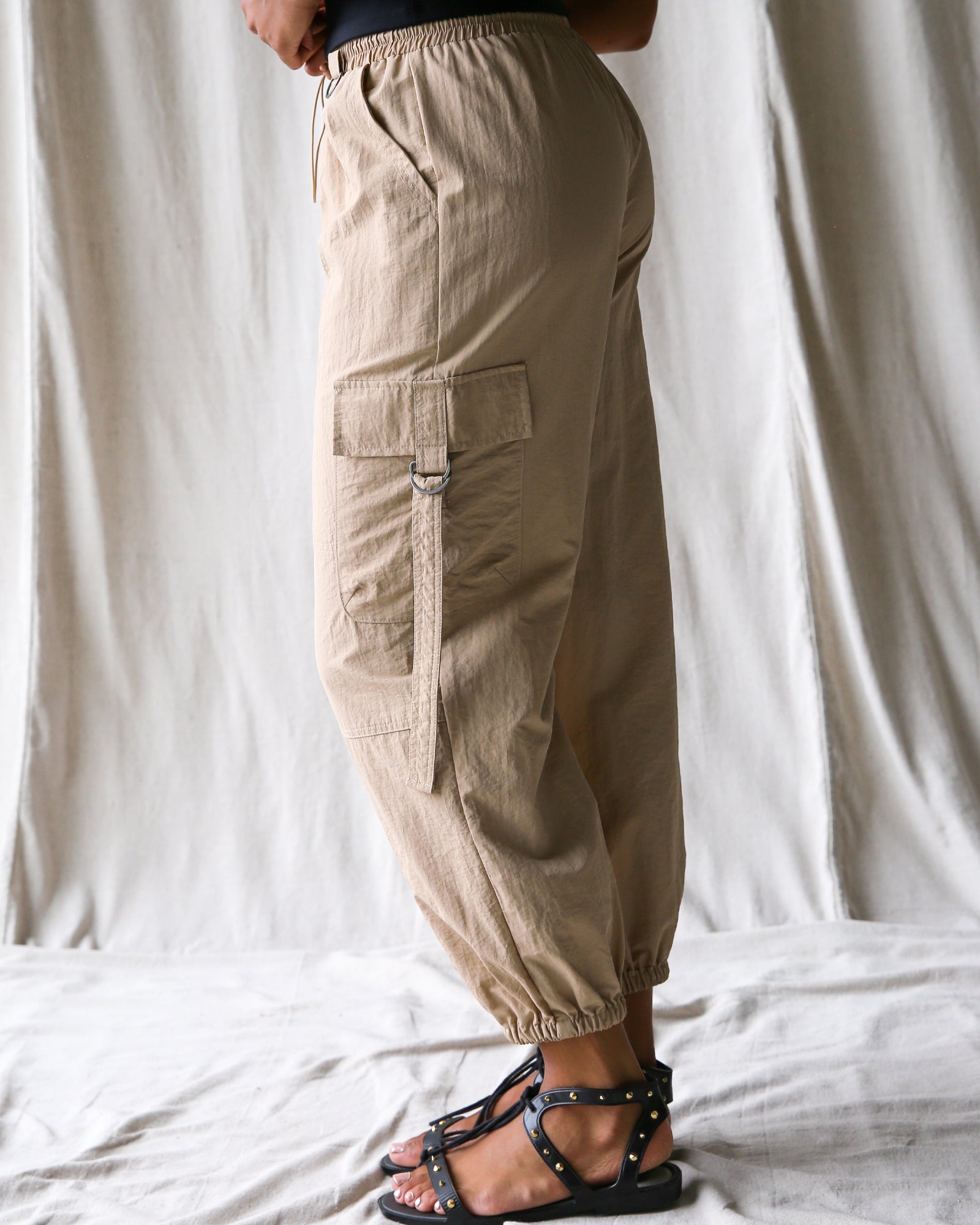 Person wearing beige cargo pants standing against a white curtain background