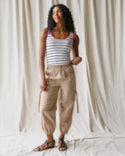 Woman wearing a striped tank top and beige cargo pants against a white curtain background
