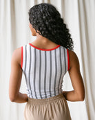 Woman wearing a striped tank top with red trim against a white curtain background