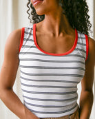 Woman wearing a white tank top with black stripes and red trim.