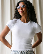 Woman wearing a white t-shirt and orange sunglasses against a neutral background