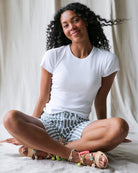 Woman sitting cross-legged on a bed wearing a white t-shirt and striped shorts.