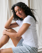 Woman sitting on a couch wearing a white t-shirt and striped shorts.