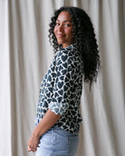 Woman wearing a patterned blouse and jeans against a neutral background