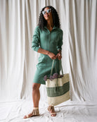 Woman in a green dress holding a striped bag against a white curtain background