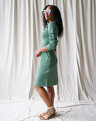Woman wearing a green dress standing against a white curtain background
