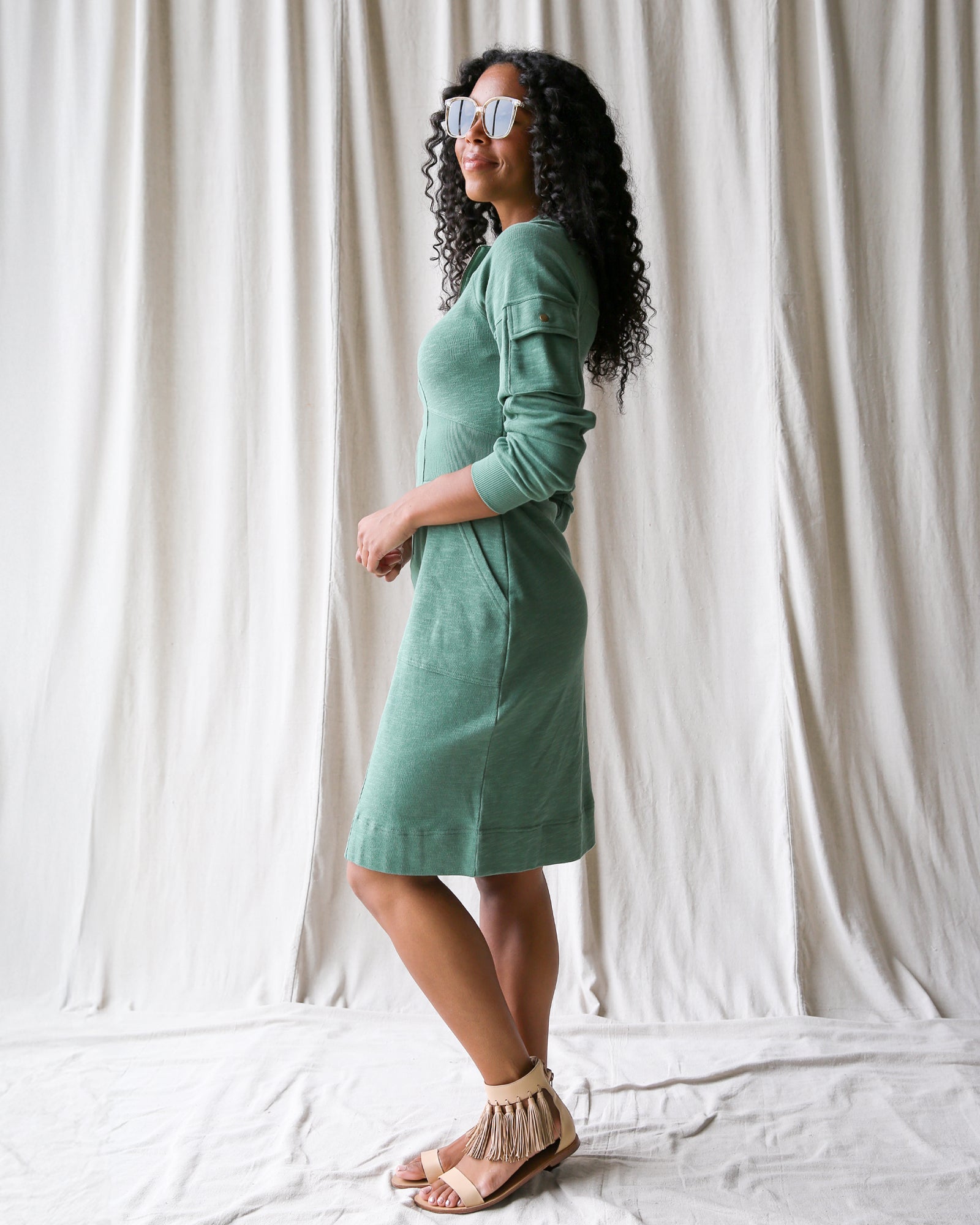 Woman wearing a green dress standing against a white curtain background