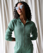 Woman wearing a green onesie against a white curtain background