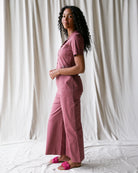 Woman wearing a pink jumpsuit standing against a white curtain.