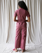 Person wearing a pink jumpsuit standing against a white curtain.