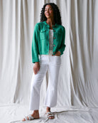 Woman wearing a green jacket and white pants against a plain background