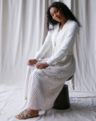 Woman wearing a white outfit with a textured skirt against a plain background