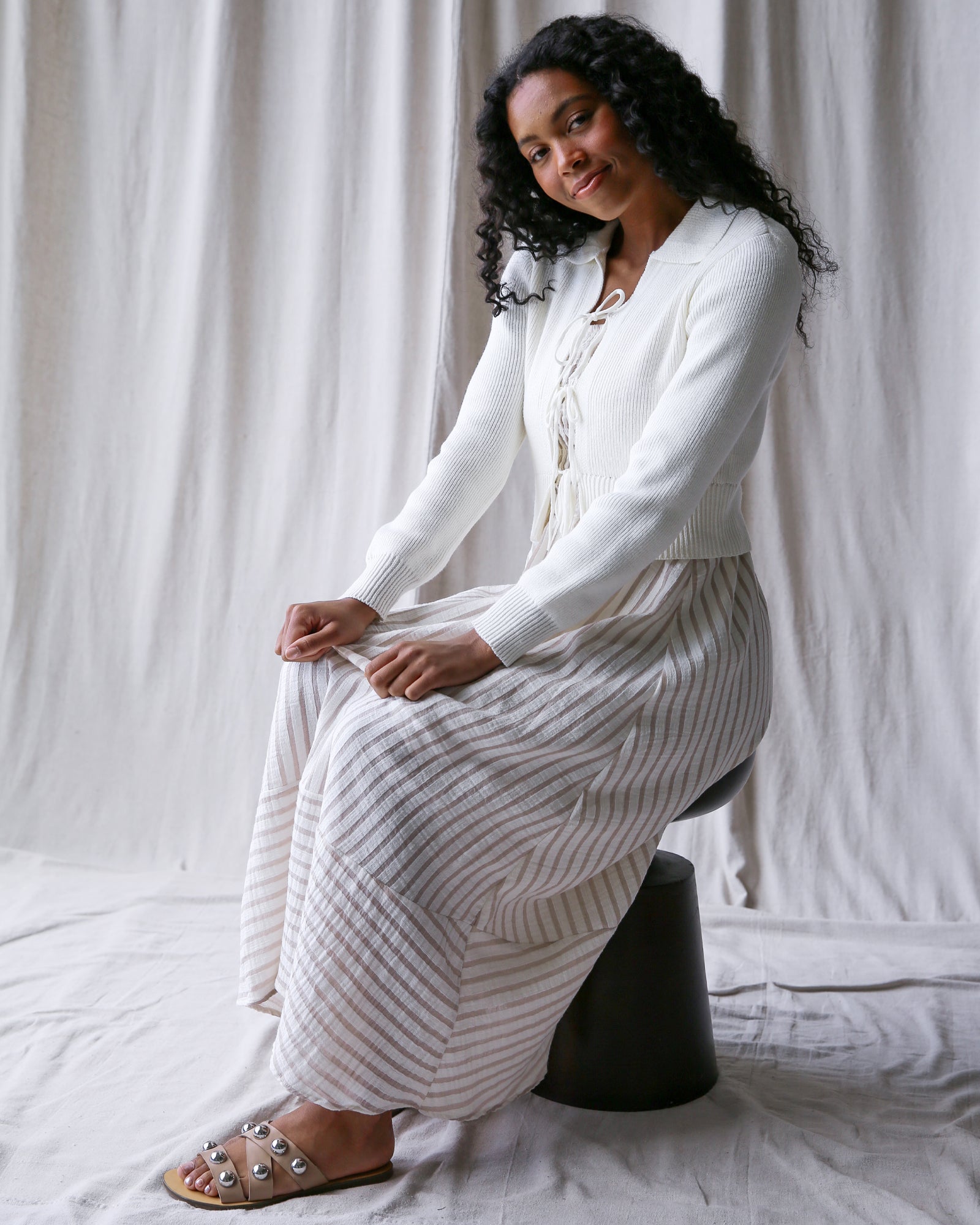 Woman wearing a white outfit with a textured skirt against a plain background