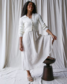 Woman wearing a white outfit with a textured skirt against a plain background