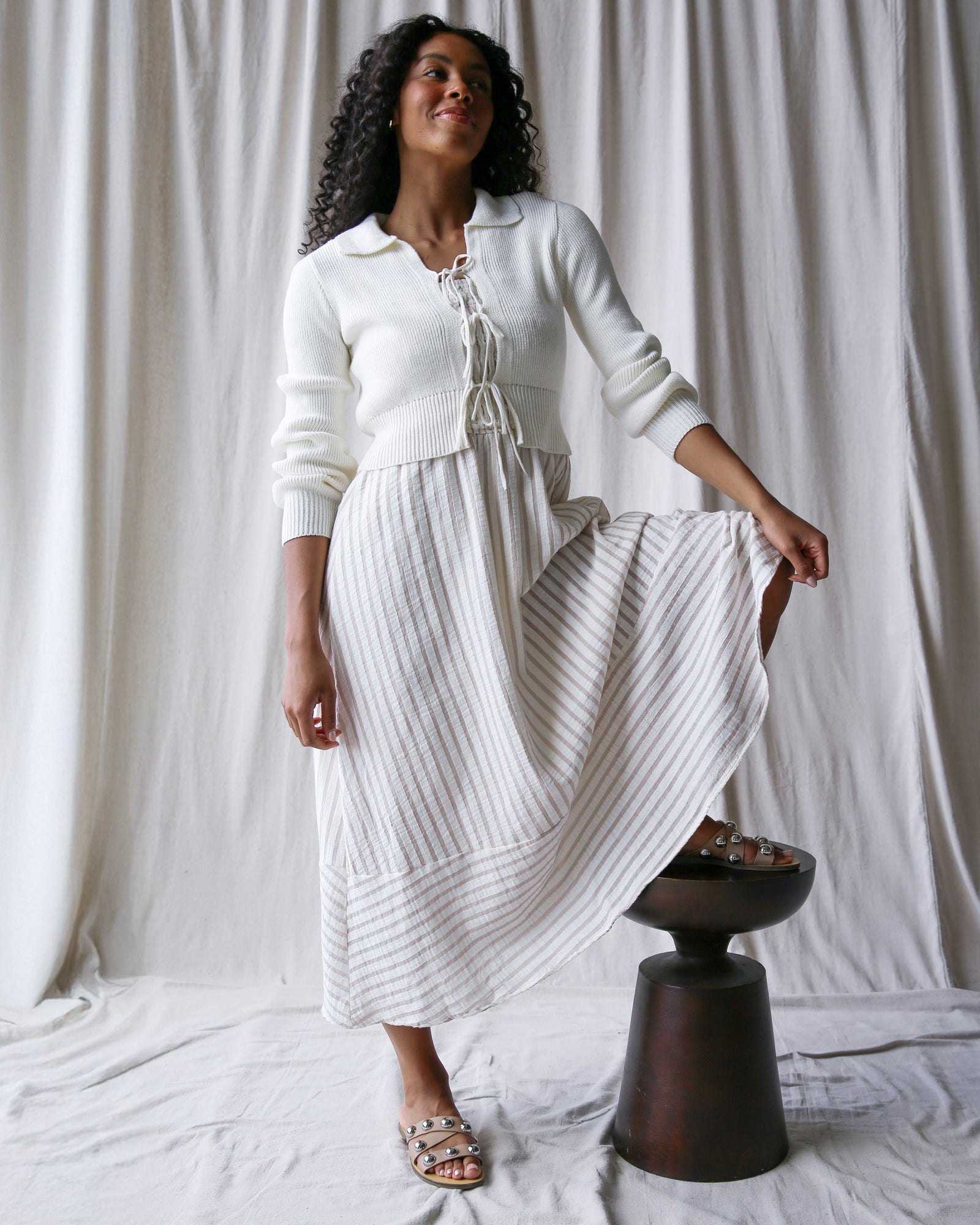Woman wearing a white outfit with a textured skirt against a plain background