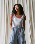 Woman wearing a striped tank top and denim pants against a plain background