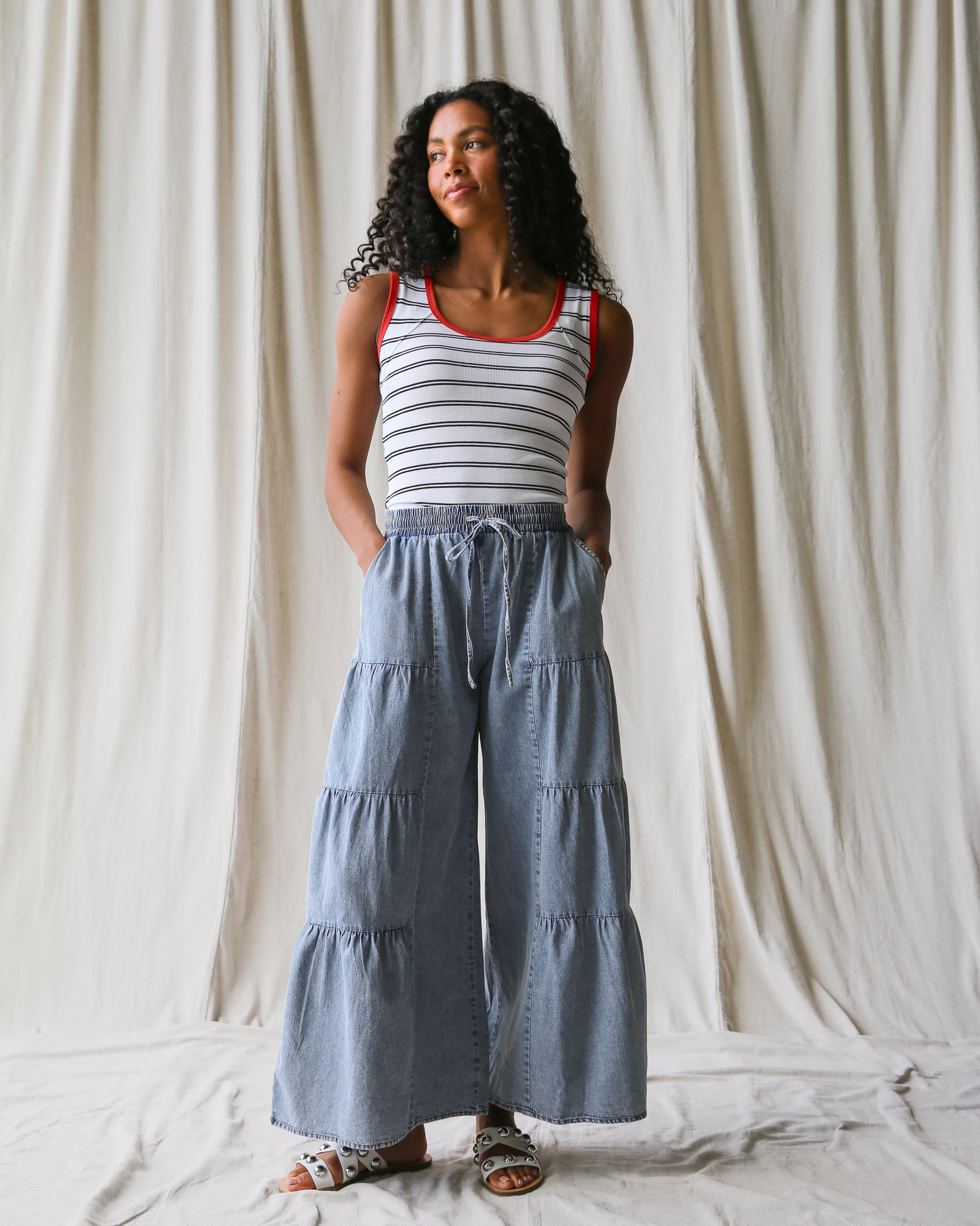 Woman wearing a striped tank top and tiered denim pants against a plain background