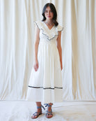 Woman wearing a white dress with black trim against a white curtain background