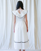 Woman wearing a white dress with black trim against a white curtain background